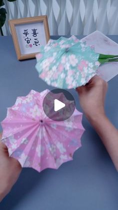 two hands holding open umbrellas on top of a blue table next to a framed picture