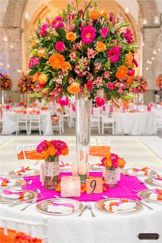 a tall vase filled with pink and orange flowers on top of a white table cloth