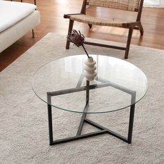 a glass table with a flower in it on a rug next to a wooden chair