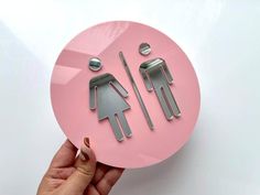 a person holding up a pink paper cut out of two men and a women's restroom sign