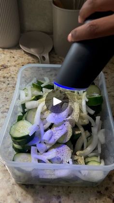 a person is pouring sauce on a salad in a plastic container with cucumbers and onions