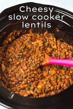 a slow cooker filled with lentils and topped with a pink spoon in it