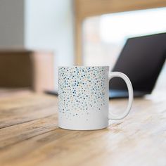 a white coffee mug sitting on top of a wooden table next to a laptop computer