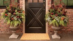 two large planters with pine cones and evergreens are on the front steps of a brick building