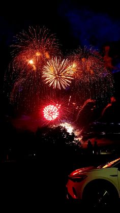 fireworks are lit up in the night sky above a car parked on the side of the road