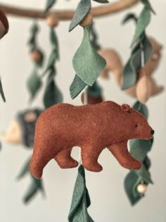 a brown bear is hanging from a branch with green leaves and other things in the background