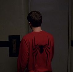 a young man in a red spider - man shirt standing next to an elevator door