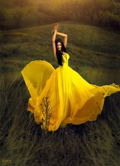 a woman in a yellow dress is standing in the grass with her arms raised up