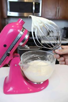 a hand holding a whisk over a pink mixer