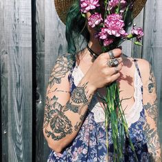 a woman with green hair wearing a straw hat and holding flowers in front of her face