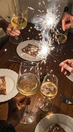 people toasting with wine and sparklers at a table filled with desserts, drinks and snacks