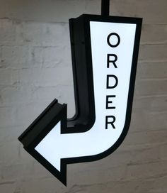 a white and black arrow sign hanging from the side of a brick wall with an order written on it