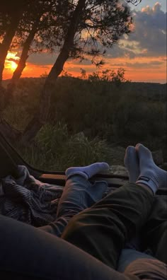 a person laying in a hammock with the sun setting behind them and trees