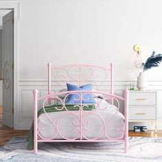 a pink metal bed frame in a white bedroom with blue and green pillows on it