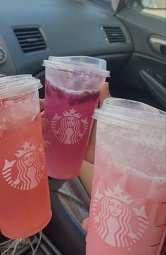 three drinks in plastic cups are being held by someone's hand while sitting in a car