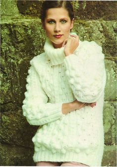 a woman in white sweater leaning against a stone wall