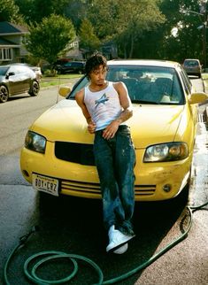 a man sitting on the hood of a yellow car with a hose attached to it