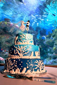 a blue and white wedding cake sitting on top of a table next to an aquarium