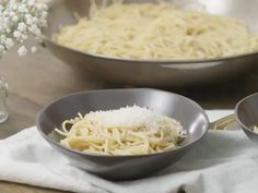 two bowls filled with pasta on top of a wooden table next to silver pans