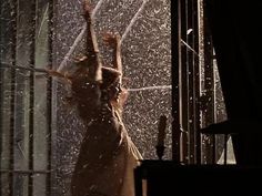 a woman standing in front of a window with water pouring from her hands and arms