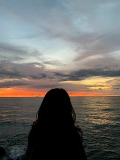 a woman standing on the edge of a boat looking out at the ocean as the sun sets