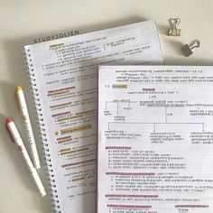 two notebooks sitting next to each other on top of a white table with pens