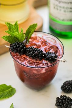 a drink with blackberries and mint garnish on the rim