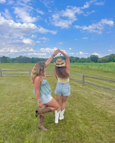 two women in short shorts and cowboy hats are standing on the grass near a fence