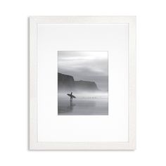 a black and white photo of a person holding a surfboard in the ocean with mountains in the background