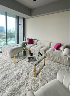 a living room filled with white furniture and large windows overlooking a cityscape in the distance