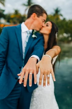 a bride and groom kissing in front of the ocean with their wedding rings on their fingers