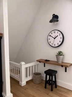 a clock mounted to the side of a wall next to a wooden table and stool