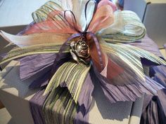 a gift wrapped in purple and green paper with a flower on top is sitting on a table