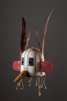 a wooden bird with feathers attached to it's head and wings hanging from the side