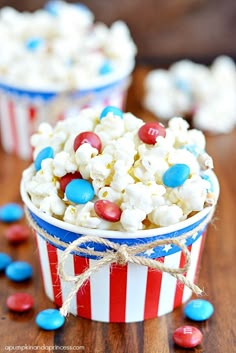 red, white and blue popcorn is in a bucket on a table with other snacks