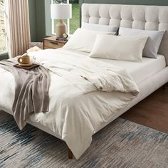 a bed with white linens and pillows in a green room next to a window