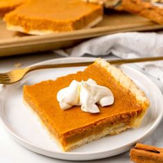 a slice of pumpkin pie on a plate with whipped cream and cinnamon sticks in the background