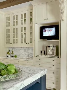 a kitchen with white cabinets and marble counter tops, television on the wall above the sink