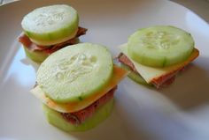 three sandwiches with cucumber slices cut in half on a white plate, ready to be eaten