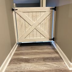 an open wooden gate in the corner of a room with hard wood flooring and gray walls