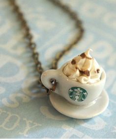 a starbucks cup necklace is shown on a blue and white tablecloth with a gold chain