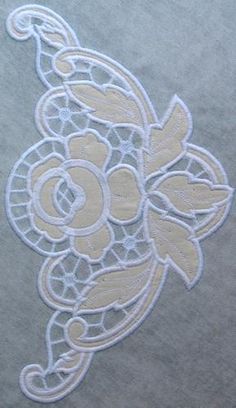 an embroidered design on the back of a gray shirt with white lace and flowers in it