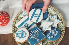 a plate with decorated cookies on it and a hand reaching for one cookie in the middle