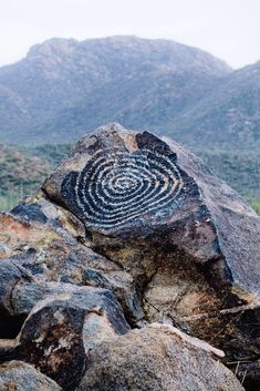 a rock with a spiral design on it in the middle of some rocks and mountains