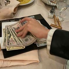 a person holding money in their hand while sitting at a table with other items on it