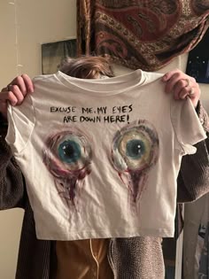 a woman holding up a t - shirt with an image of two eyes on it