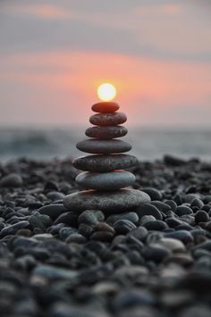 a stack of rocks sitting on top of a beach next to the ocean at sunset