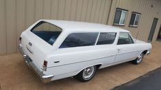 an old white station wagon is parked in front of a building with a door open