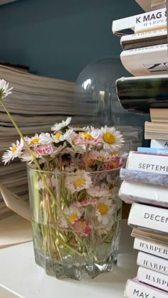 a glass vase filled with lots of flowers on top of a table next to books