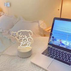 an open laptop computer sitting on top of a bed next to a light up teddy bear